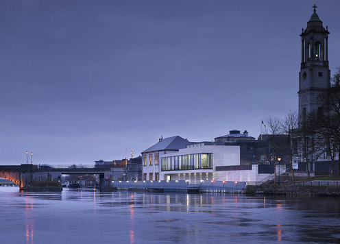 The Luan Gallery viewed upstream at dusk across the River Shannon. The tower of the church of St Peter and St Paul is silhouetted in the background.